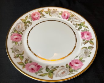 May include: A white porcelain plate with a gold rim and a floral design featuring pink and white roses. The plate has a gold band around the center.