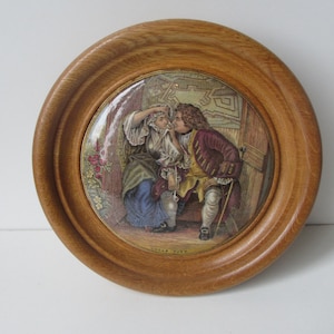 Puede incluir: Un azulejo de cerámica enmarcado con una ilustración colorida de dos personas en una habitación. El azulejo está rodeado por un marco de madera. El texto "Uncle Toby" está impreso en la parte inferior del azulejo.