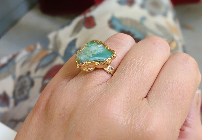 A hand wearing a Solid 14k Gold ring featuring a large raw and uncut Aqua blue Peruvian Opal