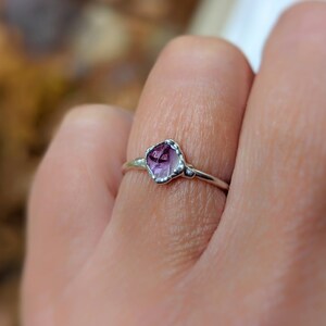 May include: A silver ring with a raw, faceted amethyst gemstone. The purple gemstone is set in a delicate, handcrafted bezel. The ring's band is thin, emphasising the unique shape and colour of the amethyst. A piece of jewellery.