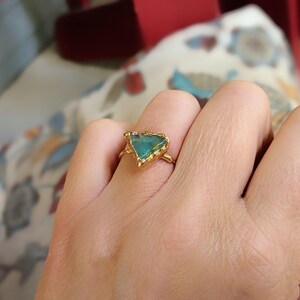 A hand wearing a Solid 14k Gold ring featuring a large raw and uncut Aqua blue Peruvian Opal