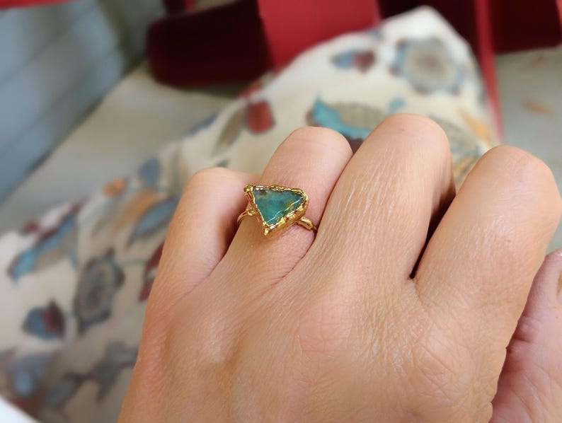 A hand wearing a Solid 14k Gold ring featuring a large raw and uncut Aqua blue Peruvian Opal