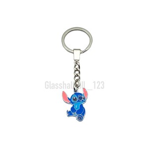 May include: A blue and pink Stitch character keychain with a silver chain and ring.