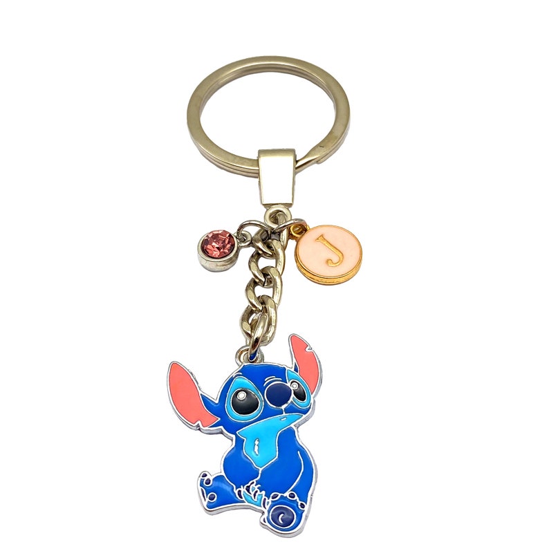 May include: Blue Stitch character keychain with a pink and gold charm with the letter J and a pink crystal charm. The keychain is attached to a silver key ring.