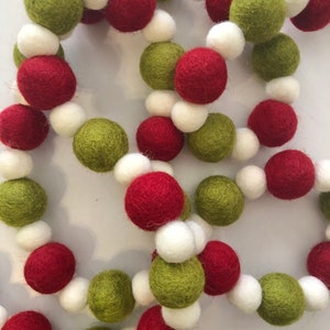 May include: A festive garland composed of felt balls in red, green, and white. The balls are strung together, creating a decorative chain. The garland is suitable for holiday or seasonal decor.
