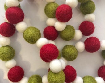 May include: A festive garland composed of felt balls in red, green, and white. The balls are strung together, creating a decorative chain. The garland is suitable for holiday or seasonal decor.