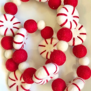May include: A festive garland featuring red and white felt ornaments. The garland includes red spheres, white spheres, and white peppermint-shaped pieces with red stripes. The arrangement is suitable for holiday or seasonal decor.