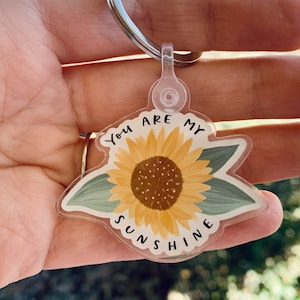 Op de afbeelding: Een transparante acryl sleutelhanger met een zonnebloem ontwerp en de tekst "You are my sunshine".