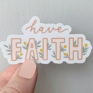 Op de afbeelding: Een witte sticker met de woorden "have faith" in cursief schrift. De woorden zijn perzikkleurig en omringd door groene bladeren en gele bloemen.