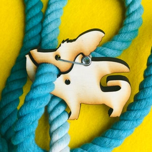 May include: A blue and white rope dog leash with a wooden dog-shaped clip attached. The clip has a metal ring for attaching to a dog collar.
