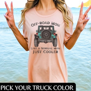 May include: A pink t-shirt with the text "OFF-ROAD MOM" and a teal jeep graphic. The text "LIKE A NORMAL MOM JUST COOLER" is below the jeep. The text "PICK YOUR TRUCK COLOR" is at the bottom of the image.