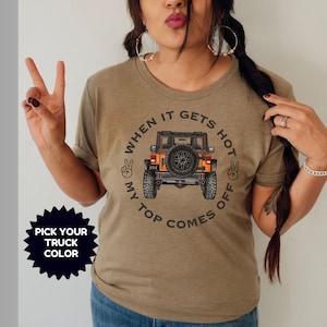 Peut inclure: Un t-shirt &agrave; manches courtes vert olive chin&eacute; avec un motif de v&eacute;hicule tout-terrain orange et une roue de secours &agrave; l'arri&egrave;re. Le texte indique "WHEN IT GETS HOT MY TOP COMES OFF" avec des signes de paix. Un graphique en &eacute;toile noir indique "PICK YOUR TRUCK COLOR".