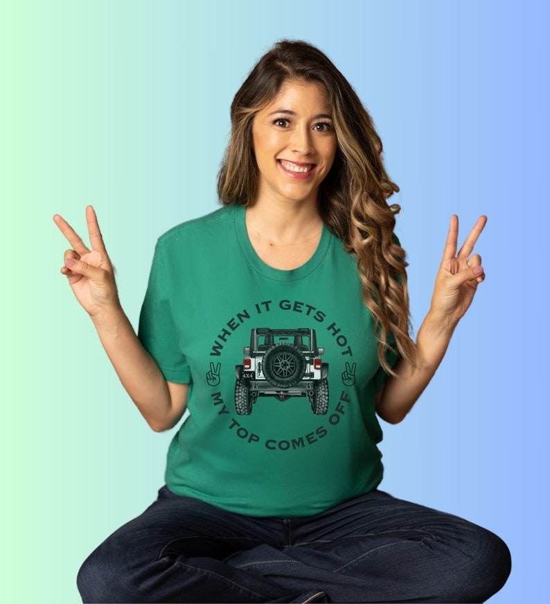 Peut inclure: Un t-shirt vert &agrave; manches courtes avec un motif repr&eacute;sentant l'arri&egrave;re d'un v&eacute;hicule tout-terrain blanc avec une roue de secours. Le texte indique "WHEN IT GETS HOT MY TOP COMES OFF" avec deux ic&ocirc;nes de signe de paix sur les c&ocirc;t&eacute;s.