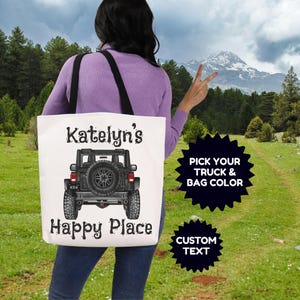 May include: A white tote bag with black straps featuring a graphic of the rear view of a black off-road vehicle. The text Katelyn's Happy Place is printed in black above and below the vehicle. Two black starburst shapes contain white text.