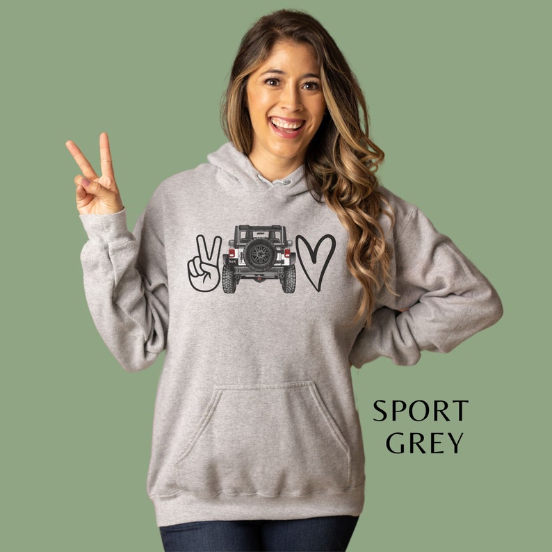 May include: A sport grey hooded sweatshirt featuring a graphic print on the chest. The design displays a peace sign, a black and white illustration of the rear view of a Jeep vehicle, and a heart shape. The text SPORT GREY is printed on the side.