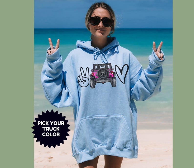 May include: A light blue hooded sweatshirt featuring a graphic print of a pink off-road vehicle positioned between a peace sign and a heart symbol. The text "PICK YOUR TRUCK COLOR" is displayed in a black starburst shape on the lower left side.