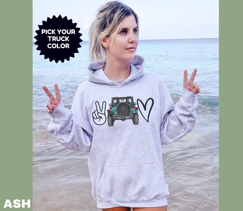 May include: A light gray hooded sweatshirt featuring a graphic print on the chest. The design includes a peace sign, a teal-colored off-road truck viewed from the rear, and a heart shape. The text PICK YOUR TRUCK COLOR is printed above.