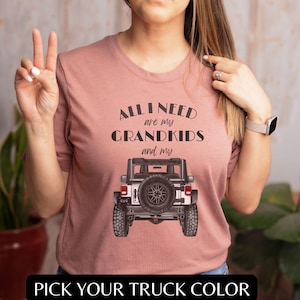 Puede incluir: Una camiseta rosa con el texto "All I need are my grandkids and my" sobre un Jeep blanco con neum&aacute;ticos negros. El texto "Pick your truck color" est&aacute; en la parte inferior de la imagen.