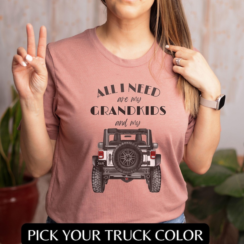 Puede incluir: Una camiseta rosa con el texto "All I need are my grandkids and my" sobre un Jeep blanco con neum&aacute;ticos negros. El texto "Pick your truck color" est&aacute; en la parte inferior de la imagen.