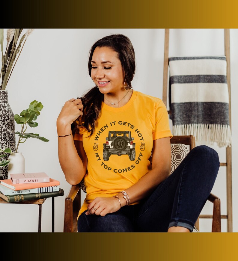 Peut inclure: Un t-shirt jaune moutarde &agrave; manches courtes avec un motif repr&eacute;sentant l'arri&egrave;re d'un v&eacute;hicule tout-terrain noir. Le texte "WHEN IT GETS HOT MY TOP COMES OFF" est imprim&eacute; en arc de cercle autour du v&eacute;hicule, avec deux ic&ocirc;nes de signe de paix.