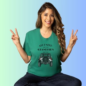 Puede incluir: Una mujer con una camiseta verde con el texto "All I need are my grandkids and my" y una ilustraci&oacute;n en blanco y negro de un Jeep. Est&aacute; sonriendo y haciendo el signo de la paz con ambas manos.