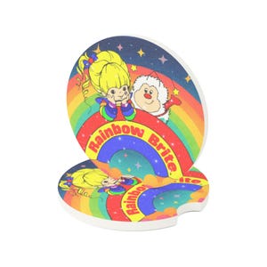May include: Two round coasters featuring a colorful design with a rainbow, stars, and the text "Rainbow Brite." The coasters depict a cartoon character with yellow hair and a smiling face. One coaster has a small notch.