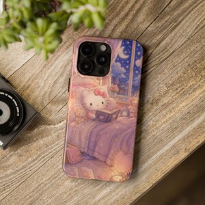 May include: A smartphone case featuring a printed illustration of a white cat character with a pink bow sitting in a bed reading a book. The scene includes a night sky with a crescent moon visible through a window, soft purple bedding, and small plush toys.