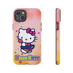 May include: A phone case with a Hello Kitty design, holding a lollipop, set against a pink and yellow gradient background with star accents. The case has a black camera module and the words "HELLO KITTY".