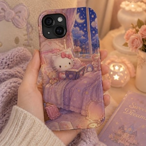 May include: A smartphone case featuring a printed illustration of a white cat character sitting in a bed reading a book. The scene includes a night sky with a crescent moon visible through a window, purple bedding, and small plush toys.