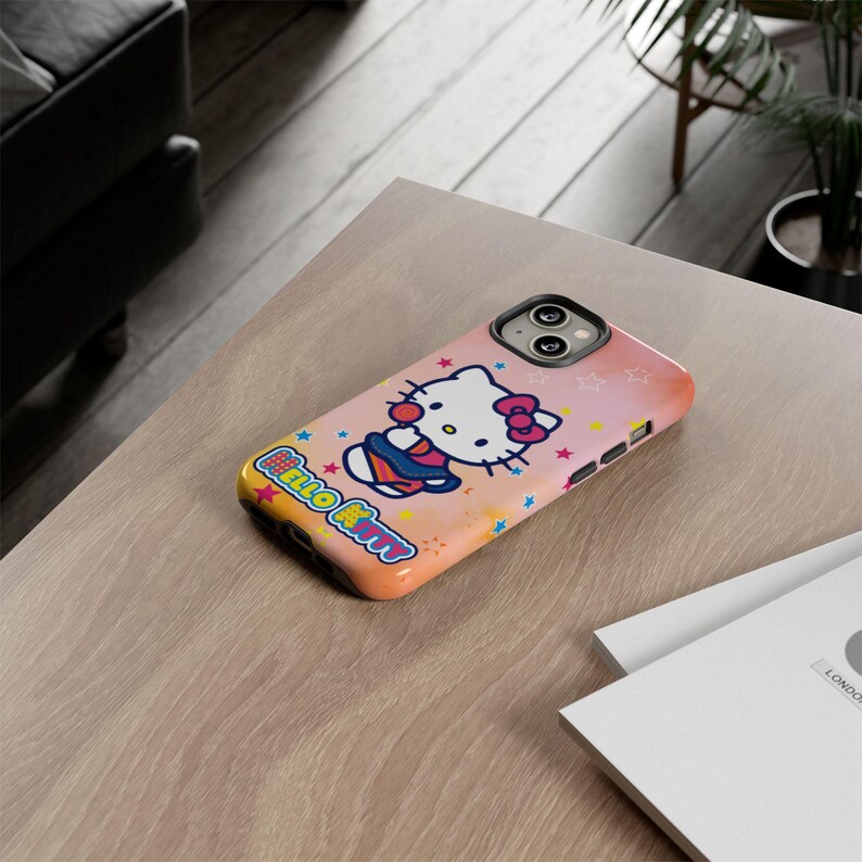 May include: A phone case with a Hello Kitty design. The case has a pink and orange gradient background with stars and a cartoon image of Hello Kitty in a basketball uniform. The text "Hello Kitty" is displayed in a colourful font.