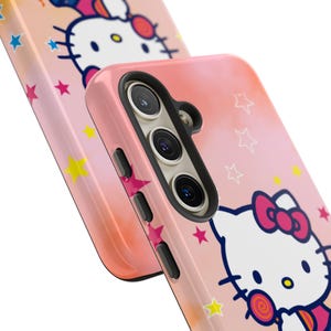 May include: Pink phone case with a cartoon cat character and a red bow, decorated with stars and a lollipop. The case has a gradient design in light pink and orange. The phone case has cutouts for the camera and buttons.