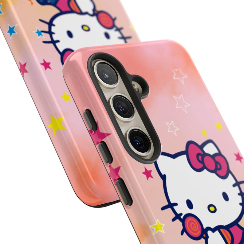 May include: Pink phone case with a cartoon cat character and a red bow, decorated with stars and a lollipop. The case has a gradient design in light pink and orange. The phone case has cutouts for the camera and buttons.