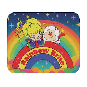 May include: A square coaster featuring a colorful illustration of Rainbow Brite and a furry creature on a rainbow. The words "Rainbow Brite" are in red and white on the rainbow. The background is a starry night sky.