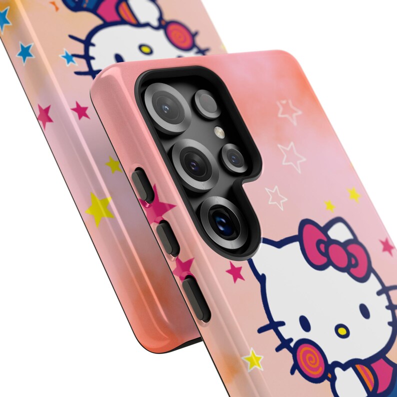 May include: Pink phone case featuring a Hello Kitty design with a bow and lollipop. The case has a gradient colour scheme and is decorated with stars. The phone case has a camera and side buttons.
