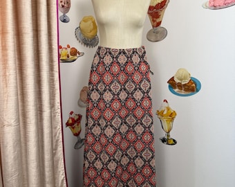 May include: A long, patterned skirt on a mannequin. The skirt features a repeating geometric design in red, black, and beige. The mannequin stands in front of a white wall decorated with ice cream sundae decals.