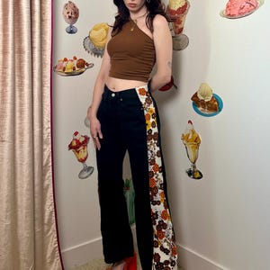 Könnte beinhalten: Eine Person trägt ein braunes Tanktop und eine schwarze Jeans mit einem floralen Muster an der Seite. Sie trägt orangefarbene Plateausandalen.