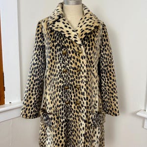 May include: A vintage leopard print coat with a double-breasted design. The coat features a classic collar, two front pockets, and gold-colored buttons. The faux fur coat is displayed on a mannequin.