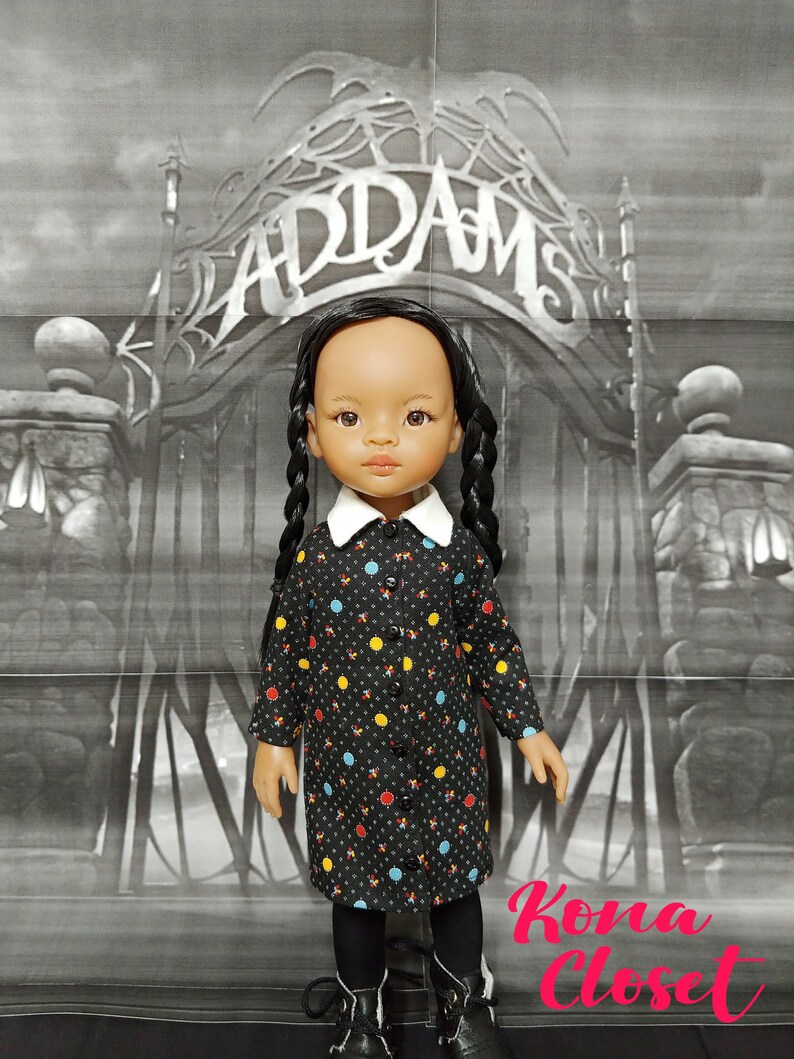 May include: A black and white doll with long black braids wearing a black dress with colorful polka dots and black tights. The doll is standing in front of a black and white backdrop with the word "Addams" written in a gothic font.