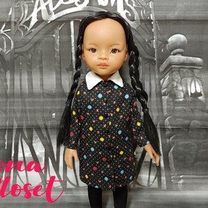 May include: A black and white polka dot dress with colorful accents. The dress has a white collar and is worn by a doll with long black braids. The doll is standing in front of a black and white background.