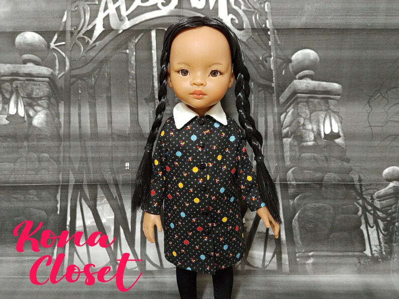 May include: A black and white polka dot dress with colorful accents. The dress has a white collar and is worn by a doll with long black braids. The doll is standing in front of a black and white background.