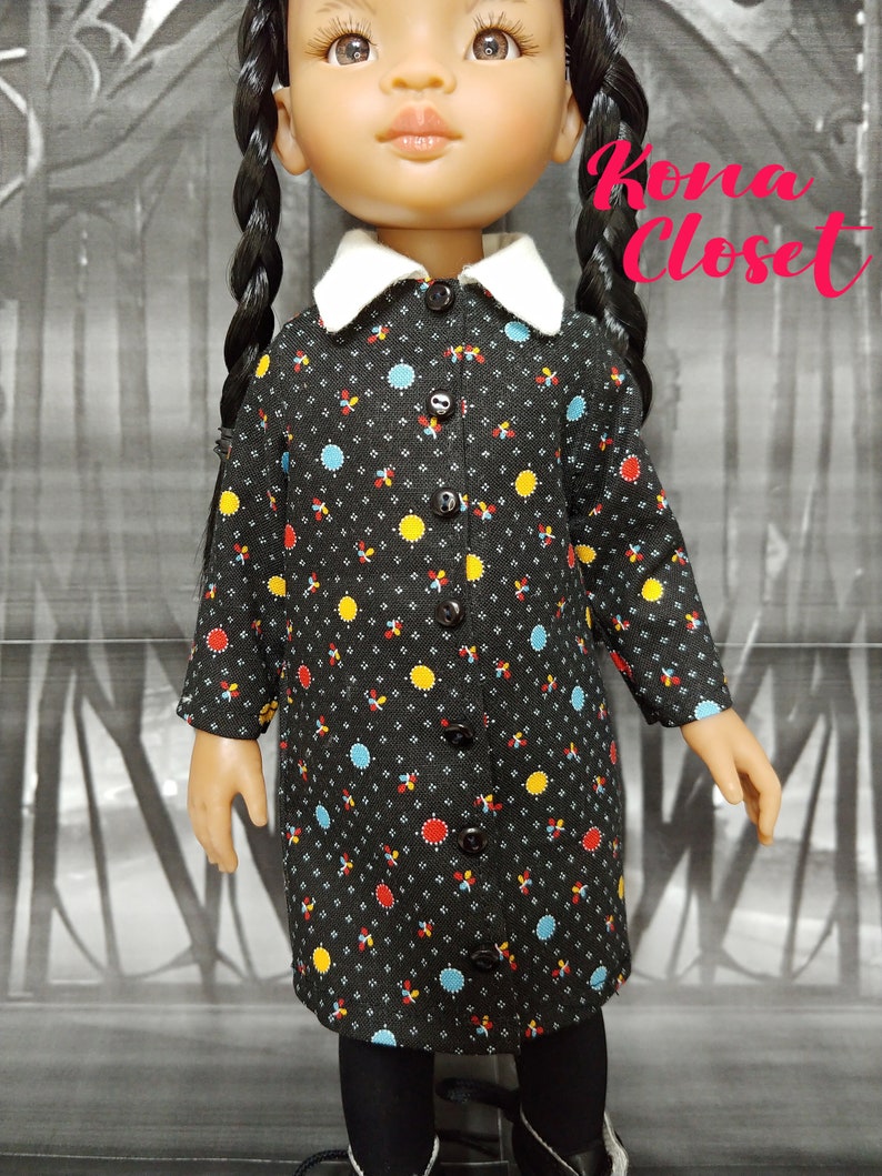 May include: A black and white polka dot dress with a white collar and button closure. The dress has yellow, red, and blue accents. Kona Closet is written in pink on the background.