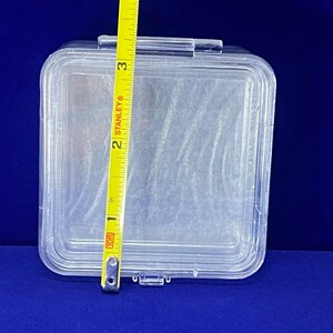May include: A clear plastic storage box with a hinged lid. The box is approximately 7.6 cm wide.