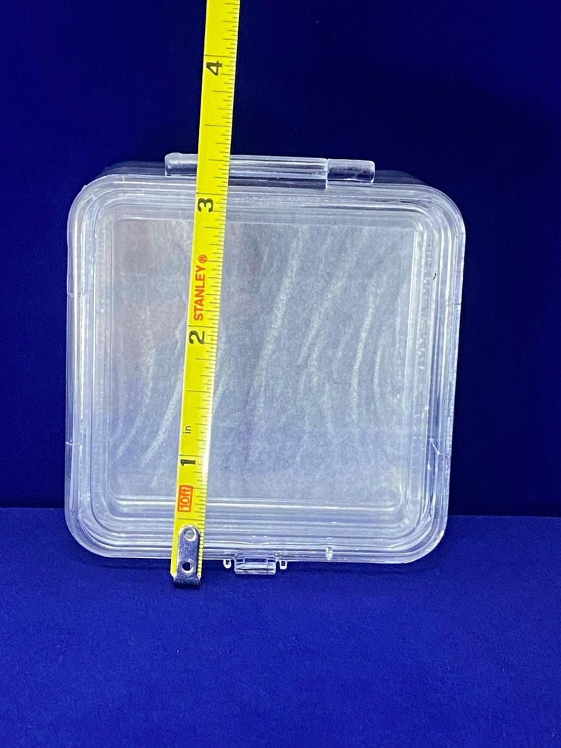 May include: A clear plastic storage box with a hinged lid. The box is approximately 7.6 cm wide.