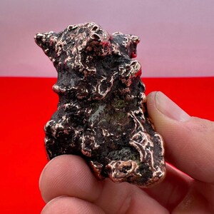 May include: A small, rough, copper sculpture with an abstract, organic shape. The sculpture has a dark, aged patina and a textured surface.