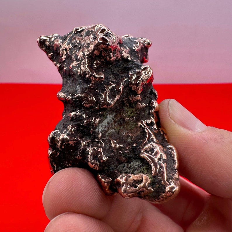 May include: A small, rough, copper sculpture with an abstract, organic shape. The sculpture has a dark, aged patina and a textured surface.