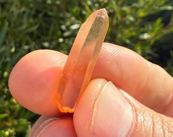 May include: A clear, orange crystal point with a pointed tip. The crystal is translucent and has a slight orange hue.