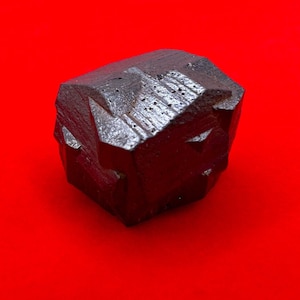 Puede incluir: Un cristal geométrico facetado de color gris oscuro con una superficie rugosa y texturizada.