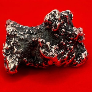 May include: A large, irregularly shaped, silver-colored rock with a rough, textured surface. The rock has a metallic sheen and appears to be made of metal.