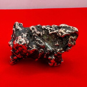May include: A silver-colored, irregularly shaped, abstract sculpture with a rough, textured surface. The sculpture is reminiscent of a rock formation.