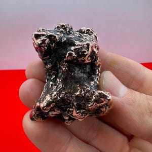 May include: A small, irregularly shaped, copper-colored metal sculpture with a rough, textured surface.